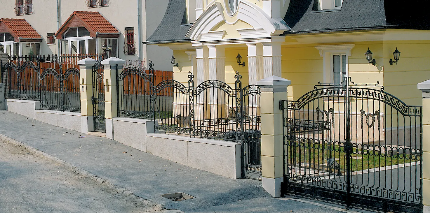 Utcakép teljes kovácsoltvas kerítés- és kapurendszerrel egy villa előtt, kis- és nagykapuval