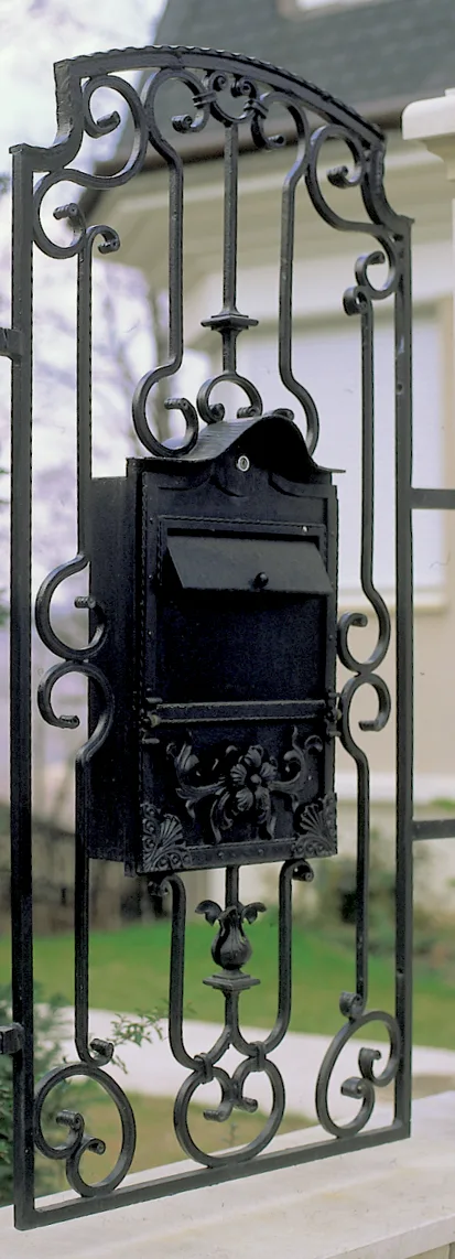Álló, keskeny kovácsoltvas mezőbe épített fekete postaláda, sátortetős fedéllel, domború levéldíszes előlappal, voluta- és levéldíszes keretben
